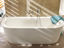 Bañera ovalada independiente de acero esmaltado junto a la pared, toalla en el borde, grifería moderna.