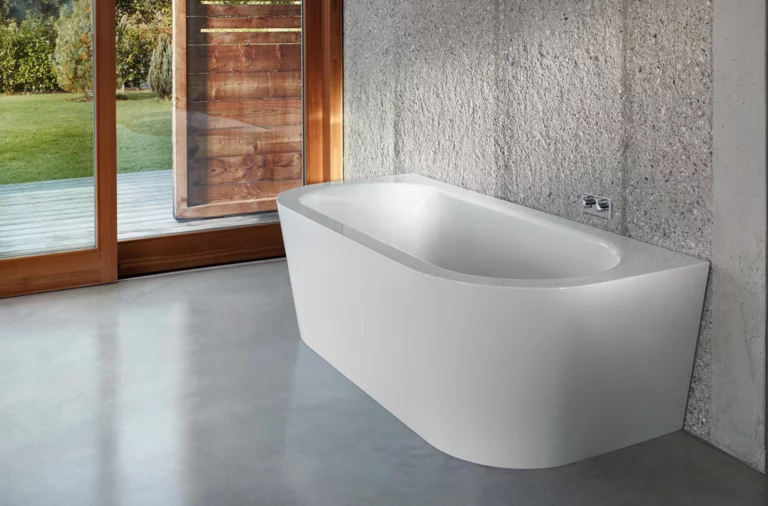 Bañera exenta de acero vitrificado, rectangular con esquinas redondeadas, sobre suelo de hormigón frente a pared de ventanas.