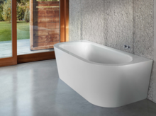 Bañera exenta de acero vitrificado, rectangular con esquinas redondeadas, sobre suelo de hormigón frente a pared de ventanas.