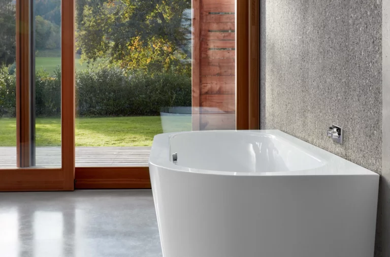 Freistehende, rechteckige Badewanne aus Stahl-Email in modernem Badezimmer mit großem Fenster und Blick ins Grüne.