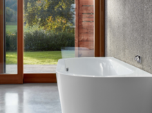 Freistehende, rechteckige Badewanne aus Stahl-Email in modernem Badezimmer mit großem Fenster und Blick ins Grüne.