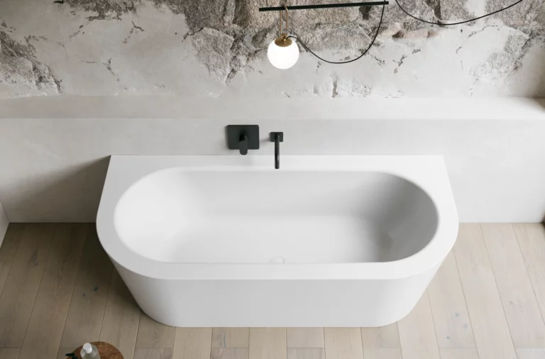 Weiße freistehende Badewanne in hellem Bad mit Natursteinoptik-Wand, schwarzer Armatur und Holzoptik-Boden.