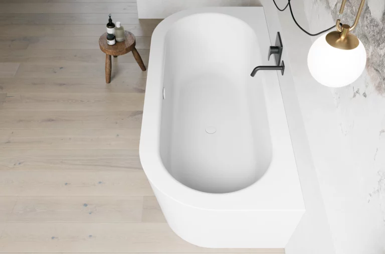 Weiße freistehende Badewanne aus Draufsicht mit schwarzer Armatur, heller Wand und Holzoptik-Boden.