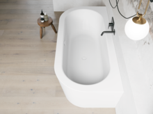 Weiße freistehende Badewanne aus Draufsicht mit schwarzer Armatur, heller Wand und Holzoptik-Boden.