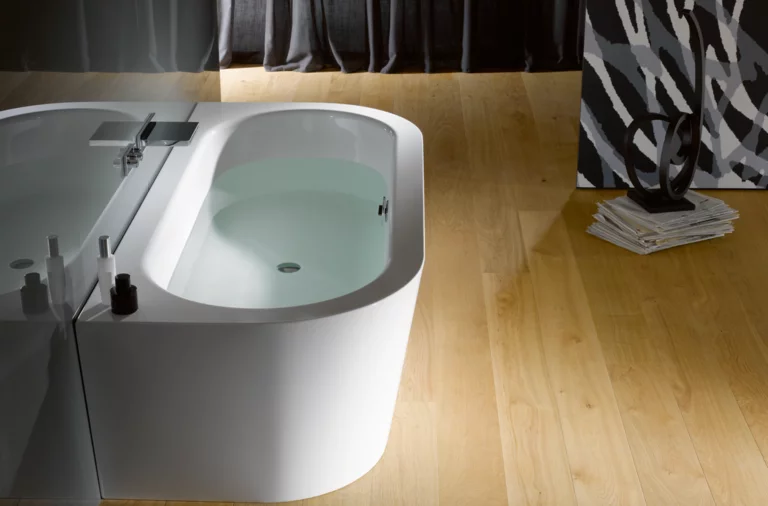 Freistehende, ovale Badewanne aus Stahl-Email mit Wasser auf hellem Holzboden, modernes Badezimmerinterieur.