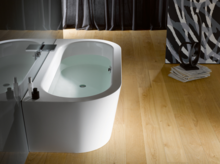 Bañera ovalada exenta de acero esmaltado con agua sobre suelo de madera clara, interior de baño moderno.