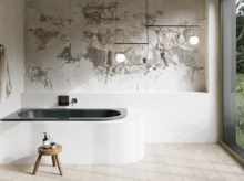 Dunkle Einbau-Badewanne in hellem Bad mit weißer Verkleidung, Natursteinoptik-Wand, Hocker und großem Fenster.