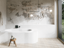 Weiße Einbau-Badewanne in hellem Bad mit Natursteinoptik-Wand, kleinem Hocker und großem Fenster.