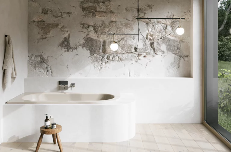 Beige Einbau-Badewanne in hellem Bad mit weißer Verkleidung, Natursteinoptik-Wand, Hocker und großem Fenster.