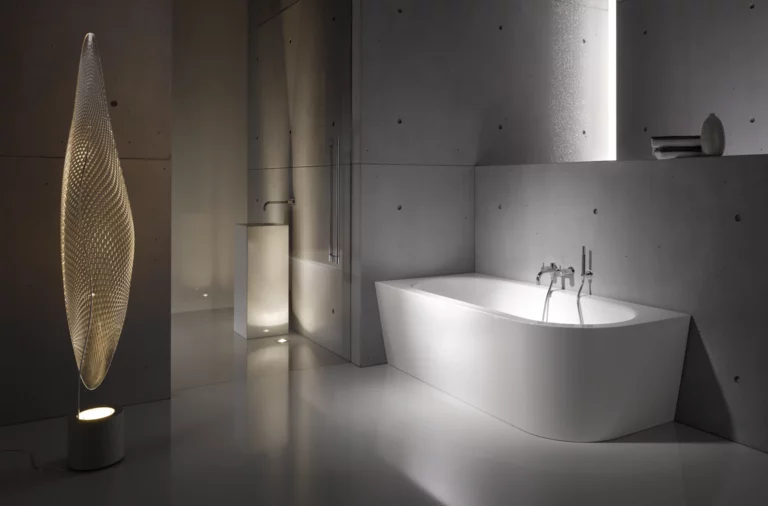 Freistehende, rechteckig-gerundete Badewanne aus Stahl-Email in modernem Bad mit minimalistischer Einrichtung und stehendem Design-Leuchtobjekt.