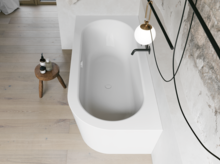 Wit inbouwbad van bovenaf in een lichte badkamer met zwarte kraan, krukje en wand in steenlook.