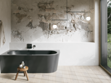 Donker inbouwbad in een lichte badkamer met wand in steenlook, krukje, handdoek en groot raam.