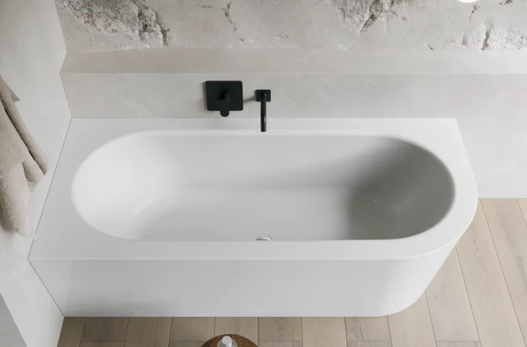 Wit inbouwbad van bovenaf in een lichte badkamer met zwarte kraan, handdoek en vloer in houtlook.