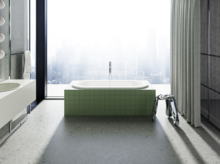 Eingelassene Badewanne mit grüner Fliesenverkleidung vor bodentiefem Fenster mit Blick auf eine nebelverhangene Stadt.