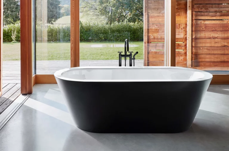 Bañera ovalada exenta de acero esmaltado en baño moderno con gran ventana y vista a la naturaleza.