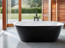 Bañera ovalada exenta de acero esmaltado en baño moderno con gran ventana y vista a la naturaleza.