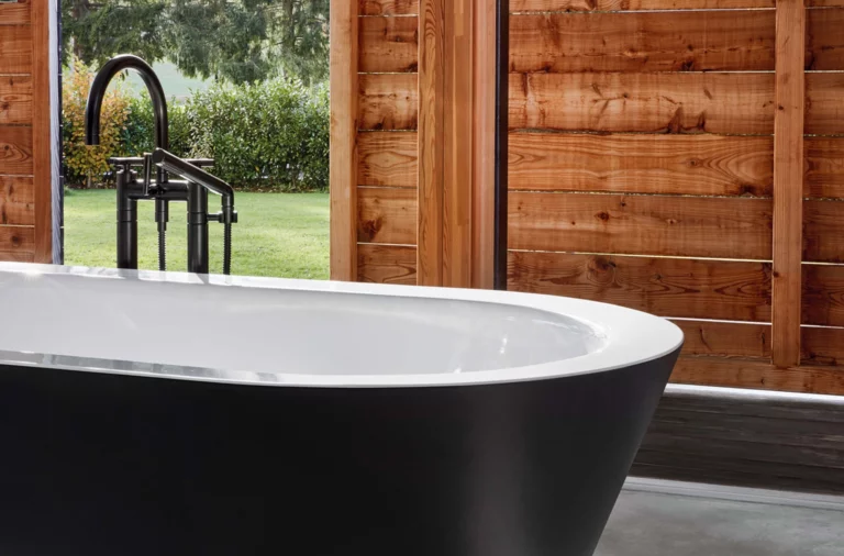 Bañera ovalada independiente de acero esmaltado con exterior negro mate frente a pared de madera.