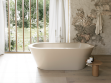 Beige freistehende Badewanne in hellem Bad mit Natursteinoptik-Wand, Beistelltisch und großem Fenster.