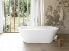 Weiße freistehende Badewanne in hellem Bad mit Natursteinoptik-Wand, Beistelltisch und großem Fenster.