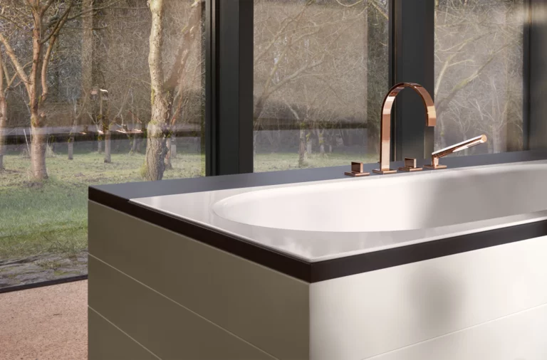 Vasca da bagno rettangolare in acciaio smaltato con angoli arrotondati, rubinetteria moderna, davanti a grandi finestre.