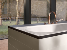 Vasca da bagno rettangolare in acciaio smaltato con angoli arrotondati, rubinetteria moderna, davanti a grandi finestre.