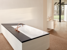 Rechteckige Stahl-Email-Badewanne mit schwarzer Umrandung, im Hintergrund Waschbecken auf weißer Einbauplatte, moderne Armaturen.