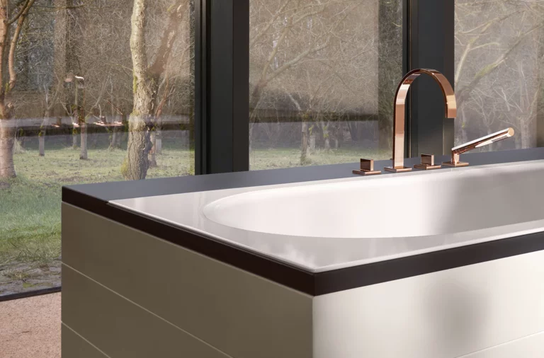 Rechteckige Badewanne aus Stahl-Email mit moderner Armatur, steht frei vor großen Fenstern mit Blick ins Grüne.