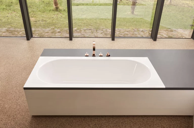 Rechteckige Stahl-Email-Badewanne mit abgerundeten Ecken, halb in eine Einbauplatte integriert, modernes Bad.