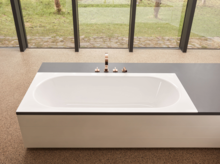 Rechteckige Stahl-Email-Badewanne mit abgerundeten Ecken, halb in eine Einbauplatte integriert, modernes Bad.