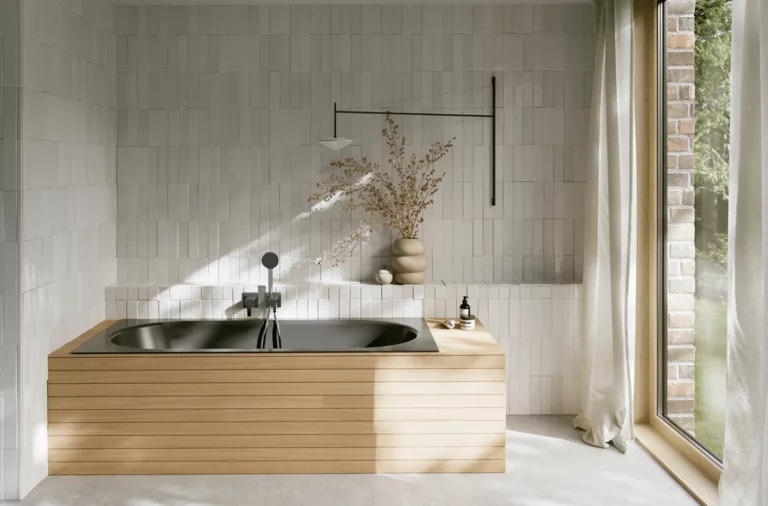 Dunkle Einbau-Badewanne in hellem Bad mit heller Verkleidung, Fliesenoptik, Vase und großem Fenster.
