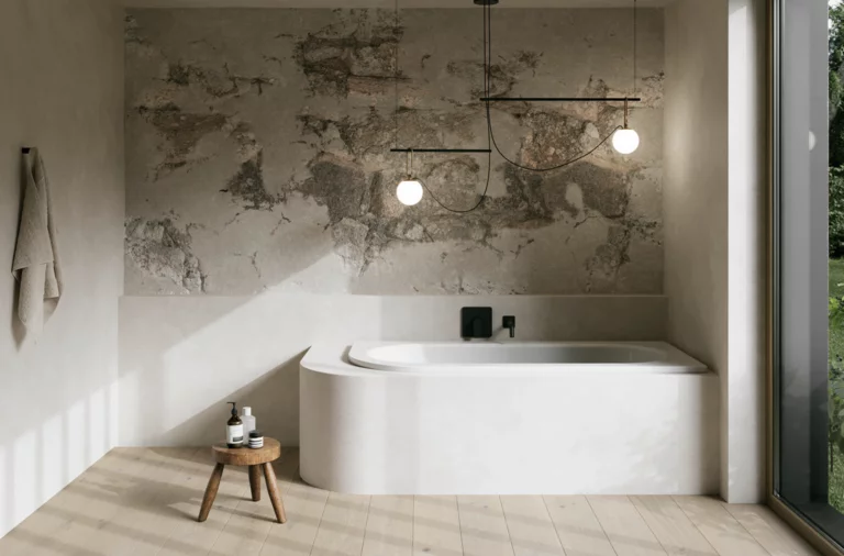 Weiße Einbau-Badewanne in hellem Bad mit Natursteinoptik-Wand, Hocker, Handtuch und großem Fenster.