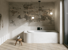 Weiße Einbau-Badewanne in hellem Bad mit Natursteinoptik-Wand, Hocker, Handtuch und großem Fenster.