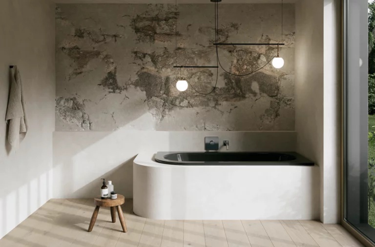 Dunkle Einbau-Badewanne in hellem Bad mit Natursteinoptik-Wand, Hocker, Handtuch und großem Fenster.