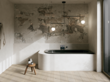 Dunkle Einbau-Badewanne in hellem Bad mit Natursteinoptik-Wand, Hocker, Handtuch und großem Fenster.