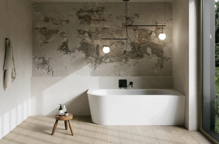 Weiße freistehende Badewanne in hellem Bad mit Natursteinoptik-Wand, Hocker, Handtuch und großem Fenster.