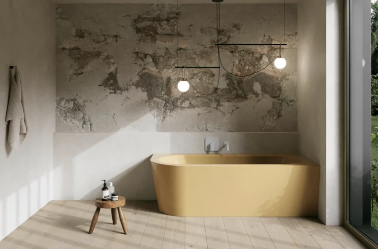 Gelbe freistehende Badewanne in hellem Bad mit Natursteinoptik-Wand, Hocker, Handtuch und großem Fenster.