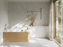 Helles Bad mit Badewanne aus glasiertem Titan-Stahl, Holzverkleidung, weißen Fliesen und großem Fenster.