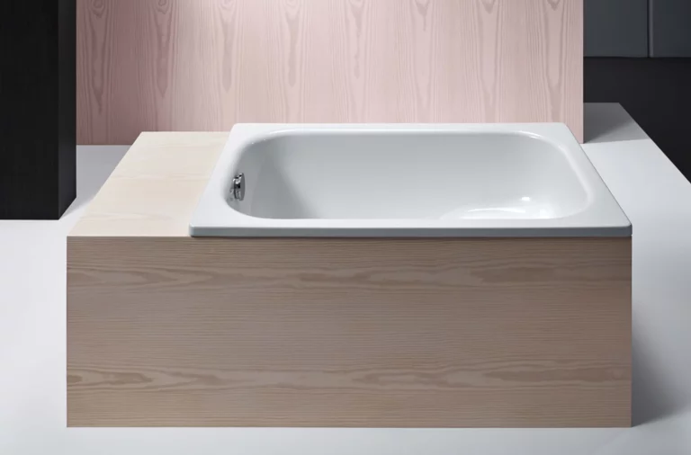 Rechteckige Badewanne aus Stahl-Email, eingebaut in eine helle Holzverkleidung, moderne und schlichte Optik.