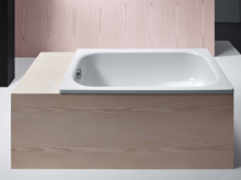 Vasca da bagno rettangolare in acciaio smaltato, incassata in un rivestimento chiaro in legno, aspetto moderno e minimalista.