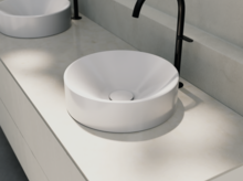 Rundes Waschbecken aus Stahl-Email auf heller Einbauplatte mit schwarzem Wasserhahn, modernes Bad-Design.