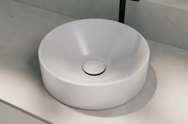 Rundes Waschbecken aus Stahl-Email auf heller Einbauplatte, moderne Armatur dahinter.