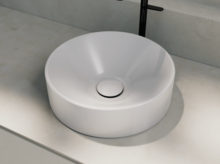 Rundes Waschbecken aus Stahl-Email auf heller Einbauplatte, moderne Armatur dahinter.