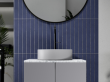 Rundes Waschbecken auf rechteckiger Einbauplatte vor blauer Fliesenwand, modernes Design, sichtbarer Wasserhahn.