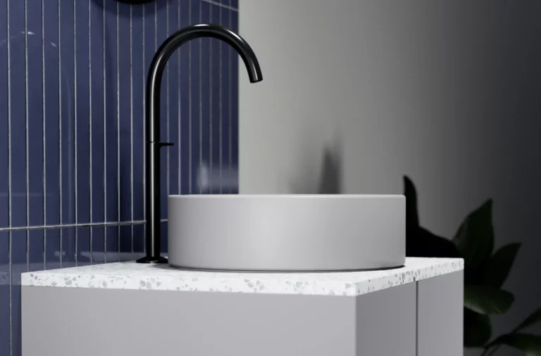 Rundes Waschbecken aus Stahl-Email auf Einbauplatte mit schwarzem Wasserhahn, blauer Fliesenwand und Pflanze im Hintergrund.