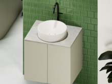 Rundes Waschbecken aus Stahl-Email auf rechteckiger Einbauplatte, vor grüner Wand, mit schwarzer Armatur.