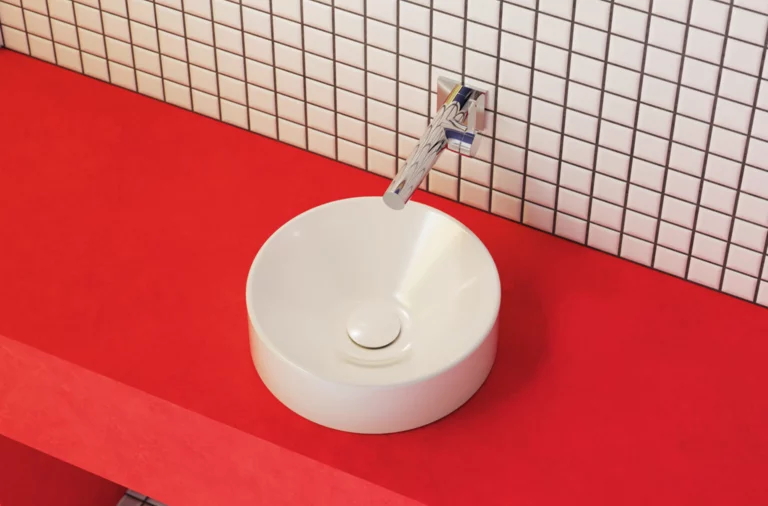 Rundes, weißes Aufsatzwaschbecken auf roter Konsole, mit Wandarmatur und weiß gekachelter Wand im Hintergrund.