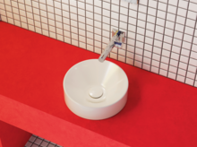 Rundes, weißes Aufsatzwaschbecken auf roter Konsole, mit Wandarmatur und weiß gekachelter Wand im Hintergrund.