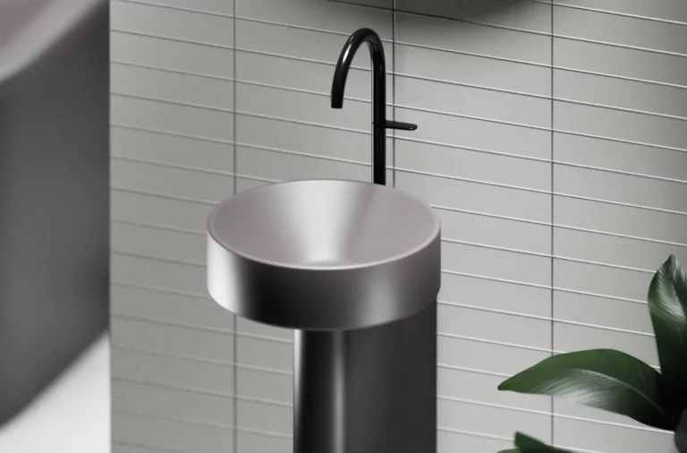 Rundes, freistehendes Stahl-Email-Waschbecken mit schwarzer Armatur vor hellen Fliesen, moderne Optik.