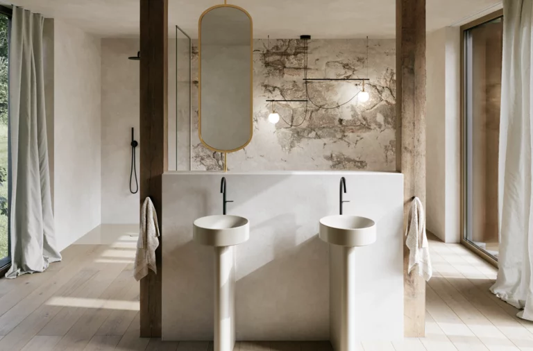 Lichte badkamer met twee beige vrijstaande wastafels, zwarte wandkranen en een grote spiegel voor een stenen wand.