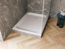 Weiße, bodengleiche Duschwanne in einer modernen Dusche mit grauer Marmoroptik und hellem Fischgrät-Holzboden.
